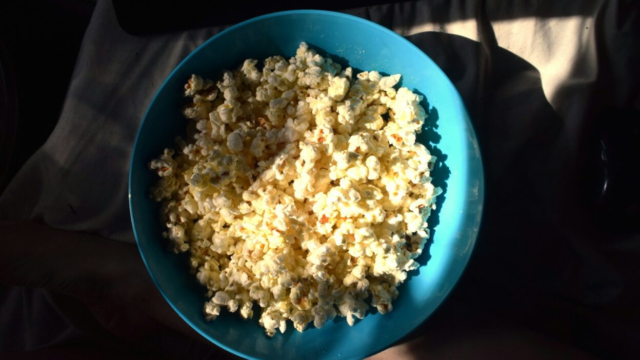 A blue bowl filled with popcorn sitting on top of a person's lap